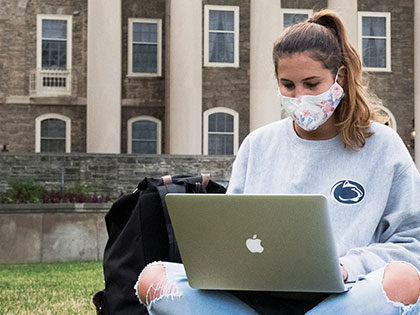 A student wearing a mask while sitting in front of Old Main