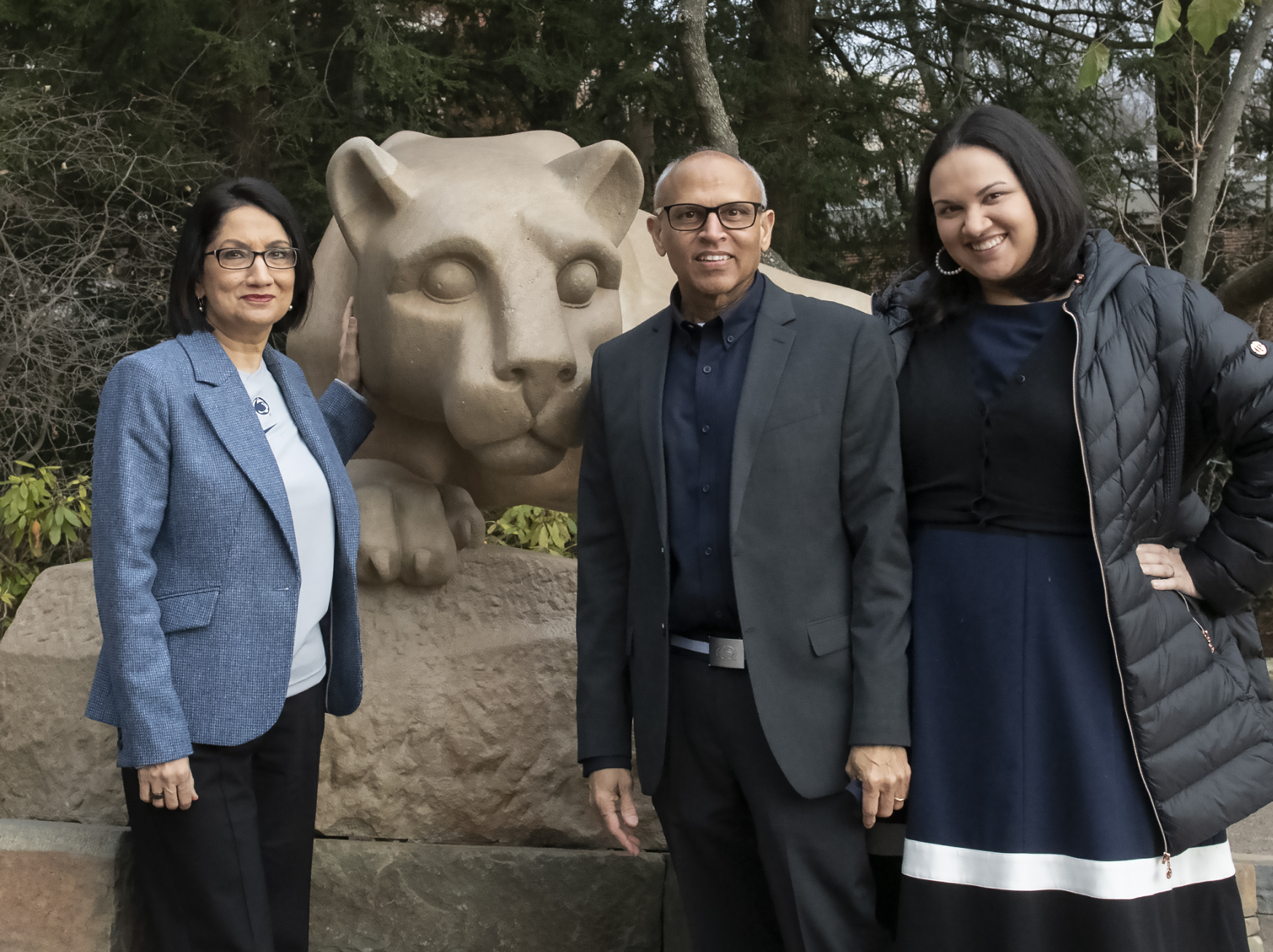 Neeli Bendapudi and her husband and adult daughter stand together in front of a stone Lion Shrine statue.