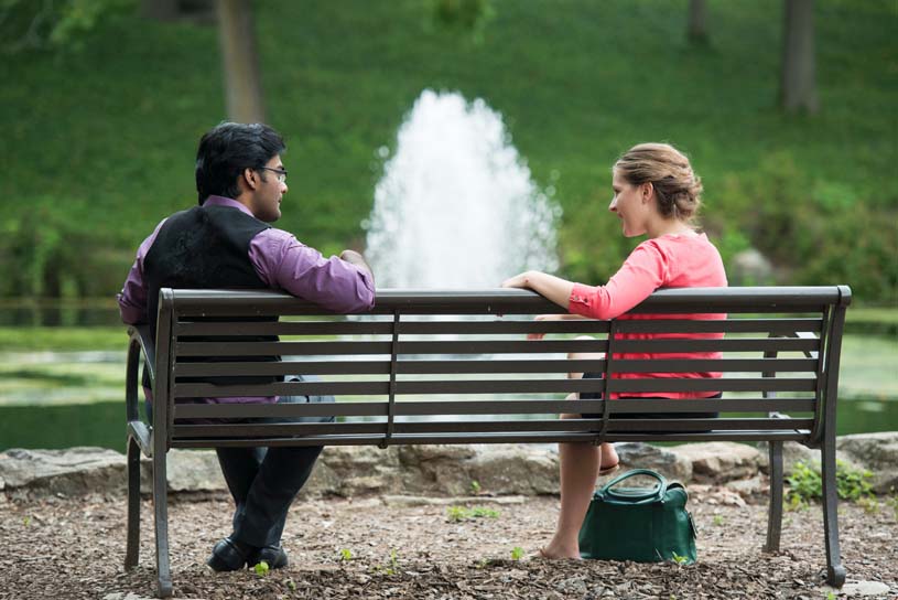 Two students talk on a bench in front of the Lares pond.