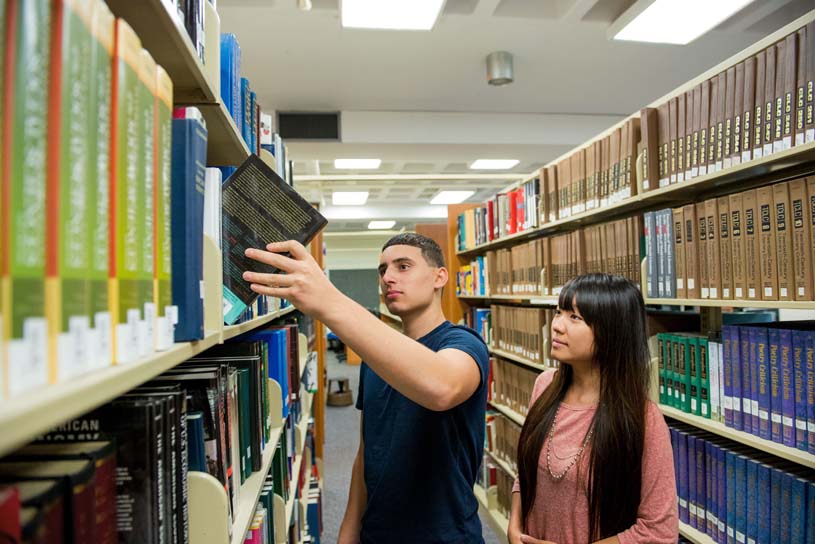 Two students reach for a book in the Abington Library