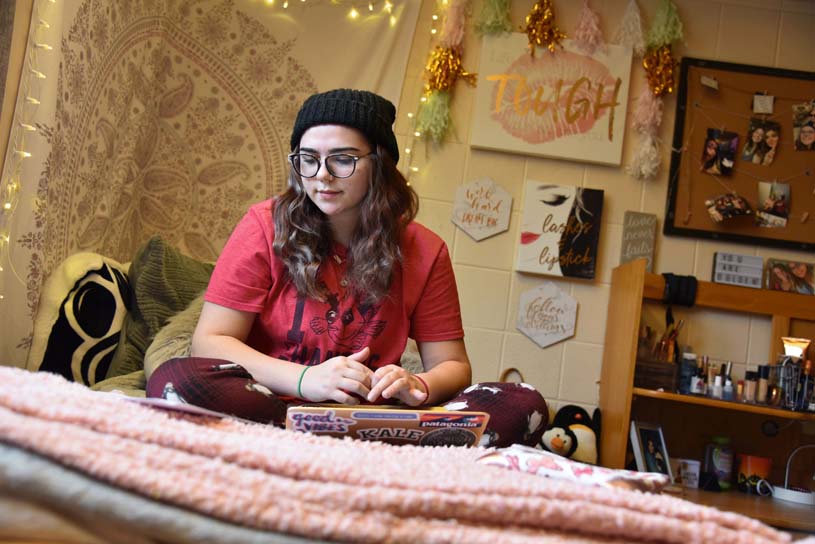 A student works on a laptop, seated on the bed of a residence hall room on the Altoona campus.