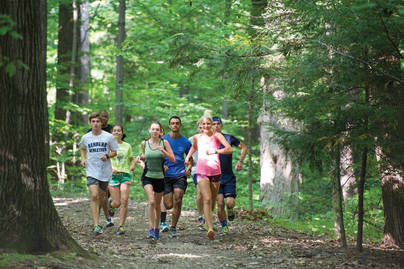 A group of nine students running on a wooded trail on the Penn State Behrend campus.