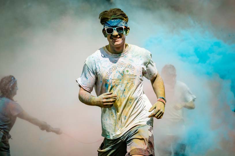 A student smiles covered in brightly colored dust smiles while participating in the Penn State Berks Color Run.
