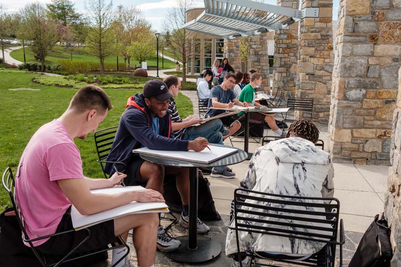 A group of students sit outside on the Berks campus drawing during an art class.