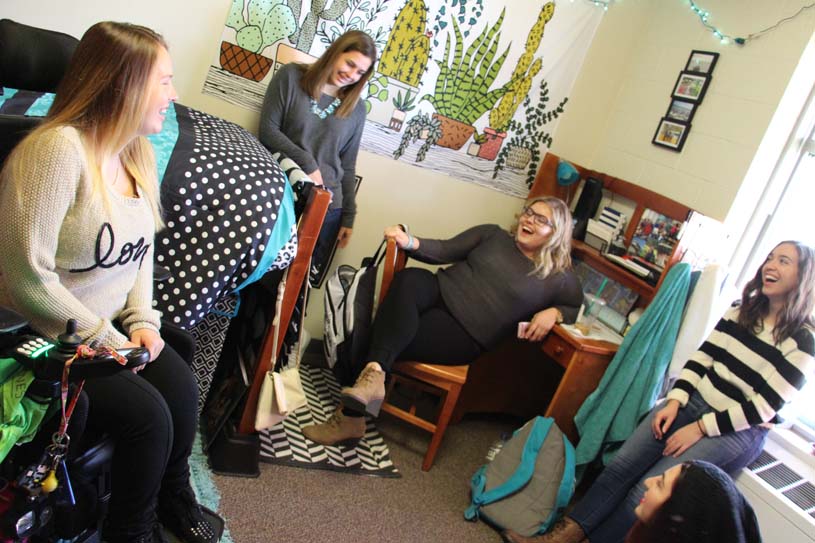 Four students talk and laugh in a residence hall room.