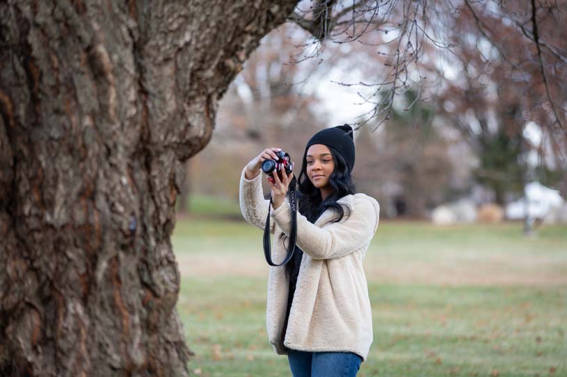 A Penn State Brandywine student with a camera taking photos of nature on campus.