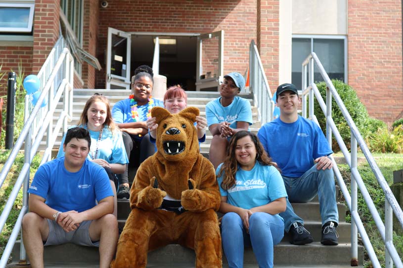 Greater Allegheny residence life staff seated around Penn State's Nittany Lion mascot on the steps leading up to McKeesport Residence Hall.