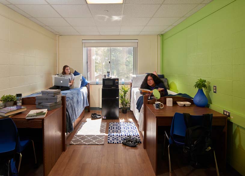 Two Greater Allegheny students study while lying on their beds in the residence hall on campus.
