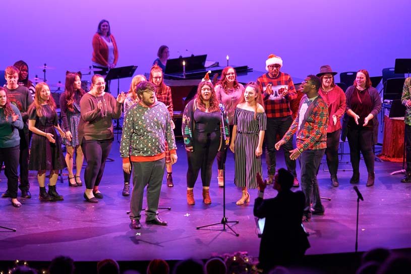 A group of Penn State Harrisburg students on stage singing during a holiday performance.