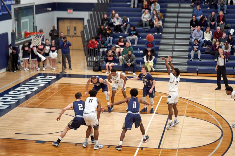 A Penn State Harrisburg men’s basketball player takes a foul shot, while other players post up and a crowd watches.