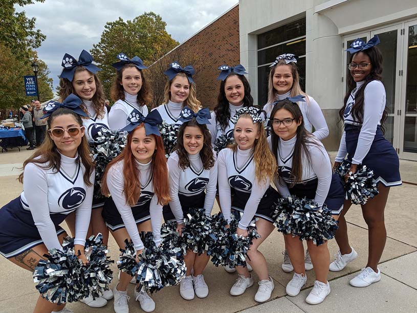 Penn State Hazleton cheerleaders with pom poms huddled together on campus mall.