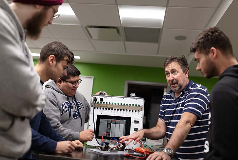 A group of Hazleton engineering students and a faculty member talk while huddled around equipment.