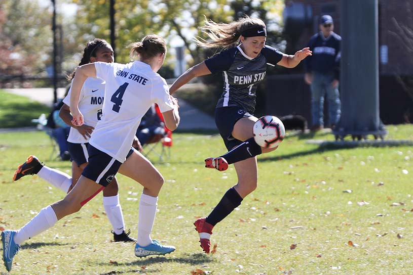 A member of the Penn State Hazleton women’s soccer team kicking ball with opposing players in pursuit.