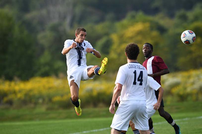 Member of the Penn State Lehigh Valley men’s soccer team in midair kicking a soccer ball.