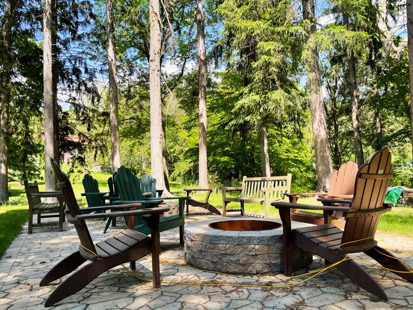 Two fire pits surrounded by Adirondack chairs under the tree canopy in the recreation area below Conklin Hall at Mont Alto.