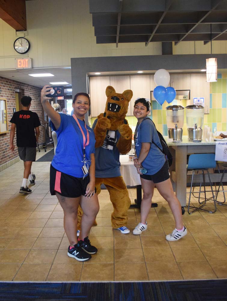 Two students take selfies with Penn State's Nittany Lion mascot in the common area of Mont Alto Hall.