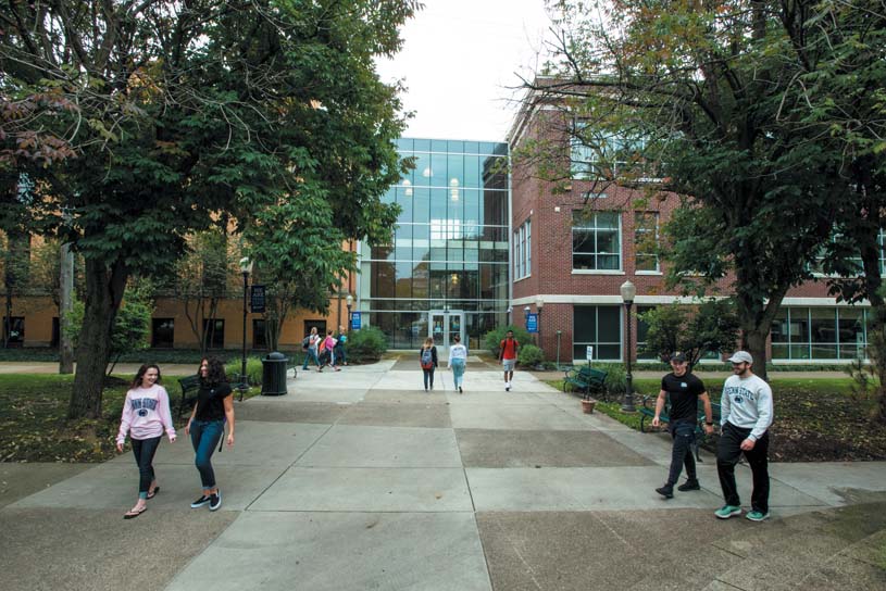 Groups of students walking on Penn State Shenango’s campus with the atrium connecting Lecture and Sharon halls in the background.