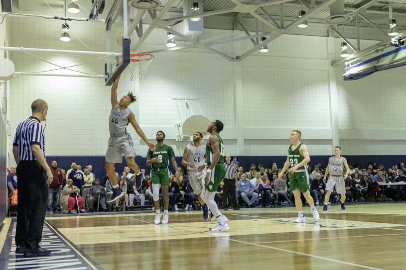 A member of the Penn State Shenango men’s basketball team goes up for a layout while other players and spectators look on.
