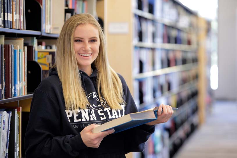 A student holding a book in the library stacks