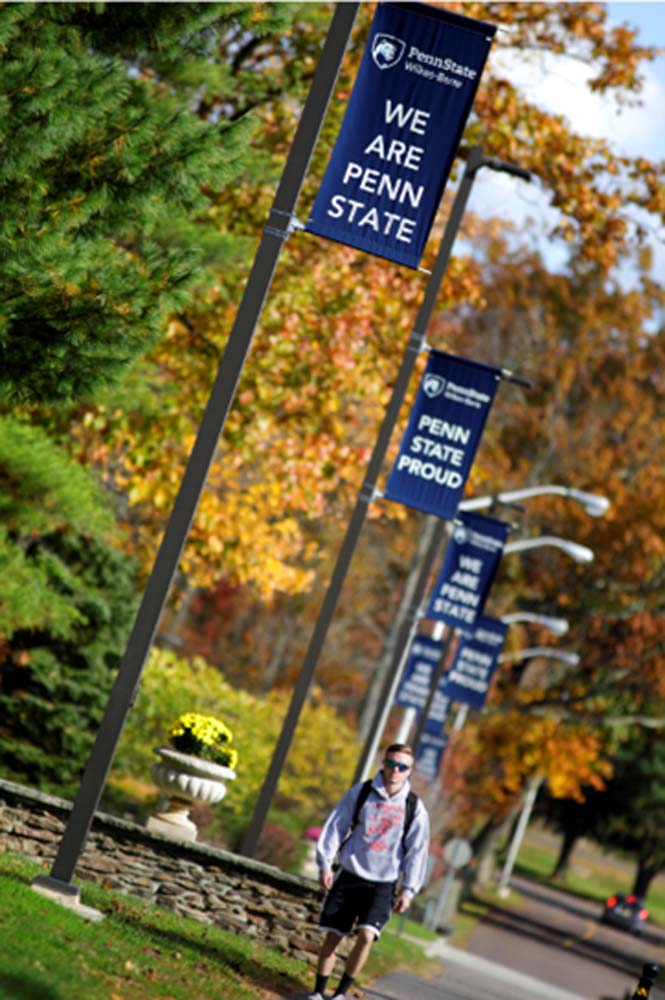 Student walking on campus under banners that read Penn State Proud