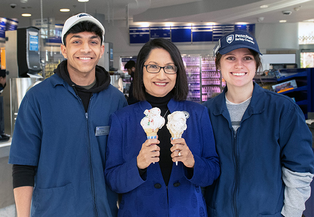 Neeli Bendapudi holds two ice cream cones and stands between two student employees who work at the Creamery.