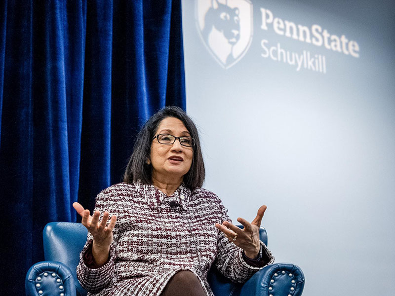 Sitting in front of a screen displaying the Penn State Schuykill logo, President Bendapudi speaks while gesturing with her hands.