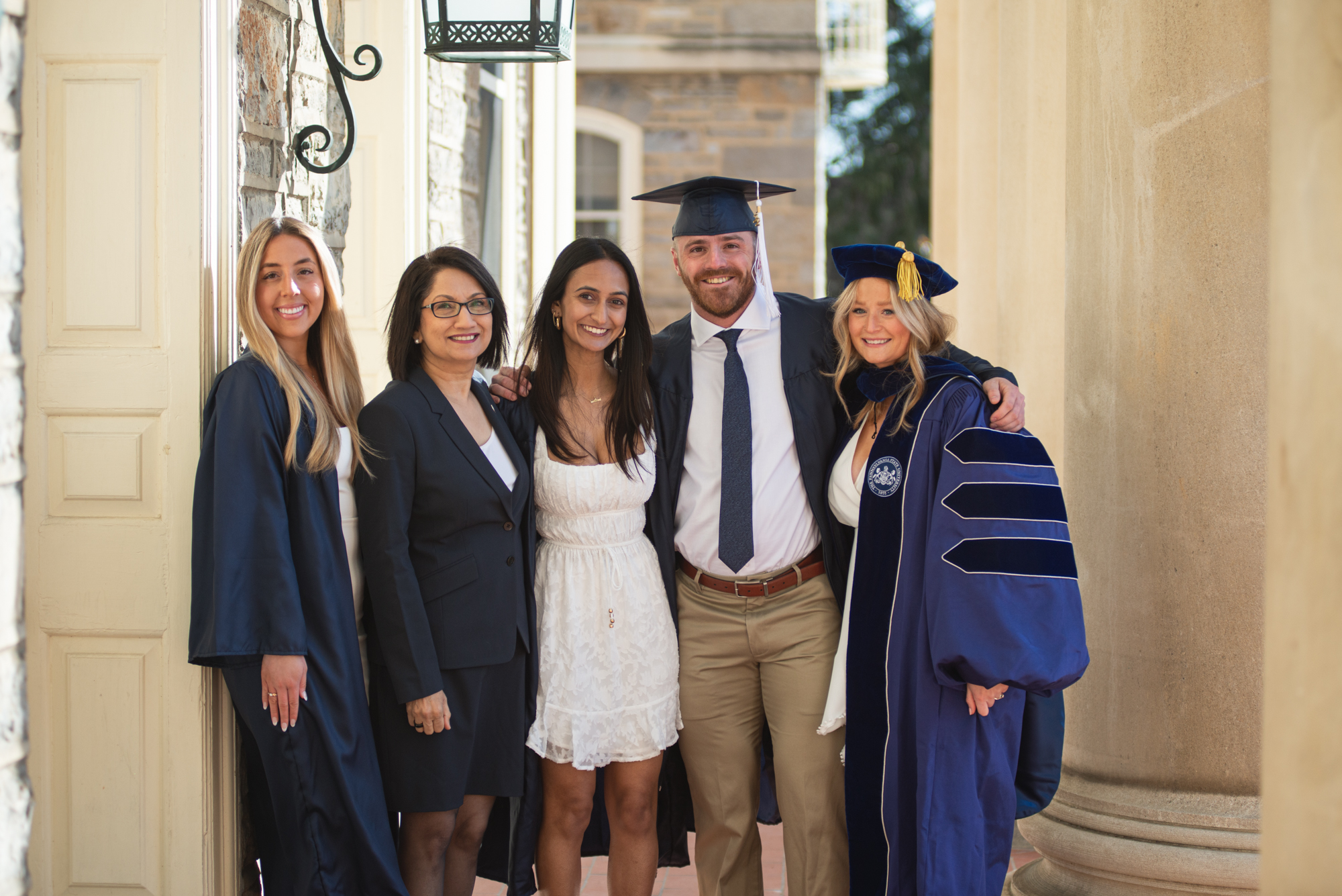 Neeli Bendapudi stands in a row with four college students dressed in graduation gaps and gowns.