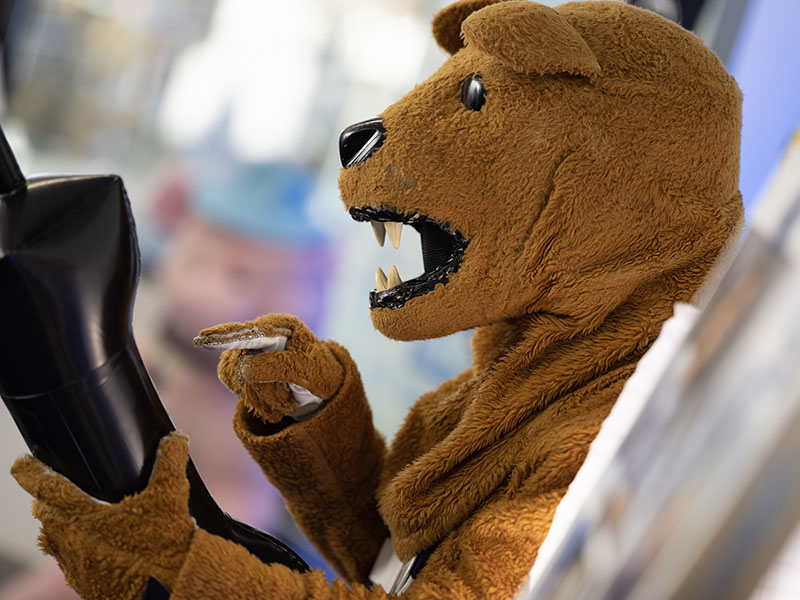 Nittany Lion Mascot pretending to dial numbers on a comically large cellphone. 