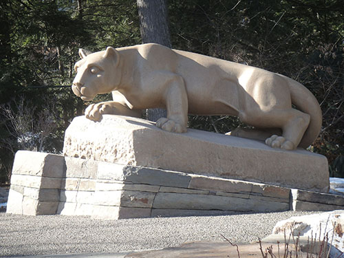A color photo of the Lion Shrine. The whole side profile of the statue is in view, on an incline of cut stones.