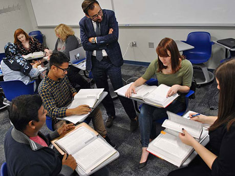 A Penn State Harrisburg faculty member stands while having a discussion with a group of seated students in a classroom on campus.