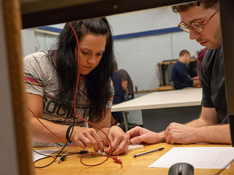 Two students work with wires in electrical engineering lab.