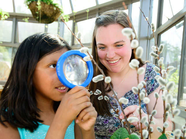 student helping a child look at a plant with a magnifying glass.
