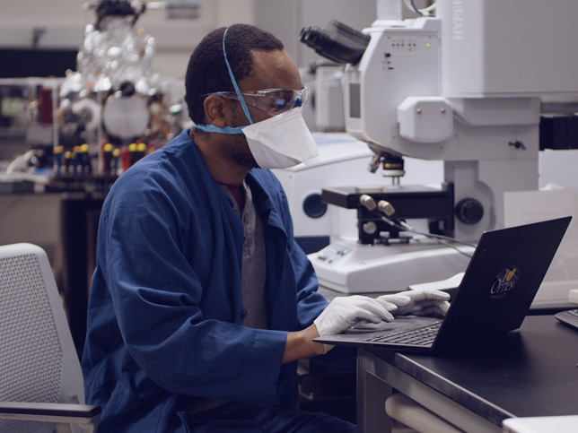 A researcher with mask at a laptop in a lab