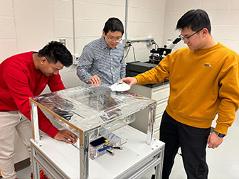 Three individuals adjust a piece of lab equipment.