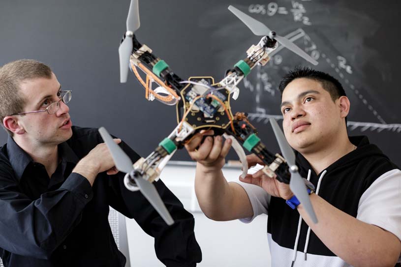 A Penn State Berks faculty member reviewing the mechanics of a drone as student holds and studies the drone.