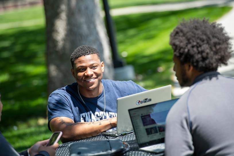 Two students sit together outdoors studying and talking on Penn State Schuylkill’s campus.